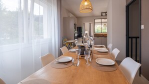 A dining area with a long wooden table set for a meal, surrounded by chairs, with a hanging light fixture above.