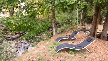 Un cadre naturel avec deux fauteuils noirs placés sur une pelouse, le tout entouré d’arbres et de rochers.