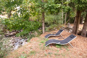 Un cadre naturel avec deux fauteuils noirs placés sur une pelouse, le tout entouré d’arbres et de rochers.
