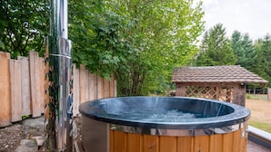 A hot tub with a wooden exterior, surrounded by a wooden fence and trees.