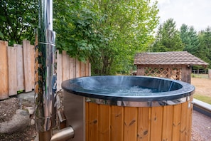 Un bain à remous avec une structure extérieure en bois, entouré d’une clôture en bois et d’arbres.