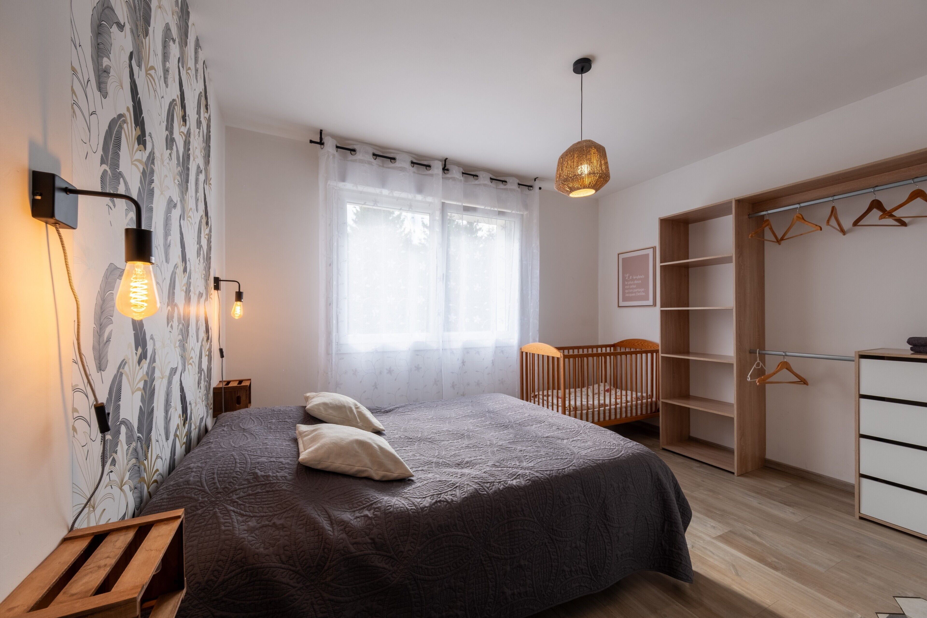 Ett sovrum med en säng, sänglampor, en spjälsäng, en garderob och en hängande taklampa.