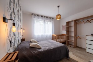 A bedroom with a bed, bedside lamps, a crib, a wardrobe, and a hanging light fixture.