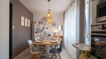 Un espace repas moderne avec une table en bois dressée pour quatre personnes, entourée de chaises, d’un luminaire suspendu et d’un mur orné d’une fresque florale.