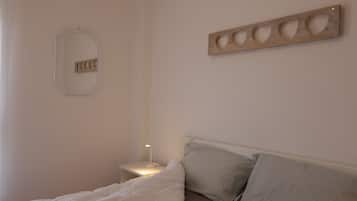 A bedroom with a bed, a bedside table with a lamp, a wall-mounted mirror, and a wooden art piece.