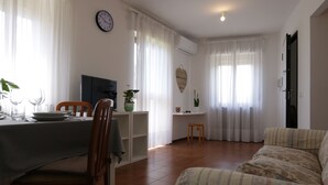 A dining area with a table set for two, a sofa, and a clock on the wall.