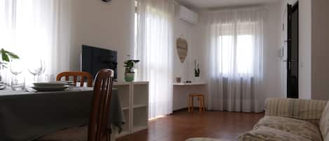 Un comedor con una mesa dispuesta para dos personas, un sofá y un reloj en la pared.