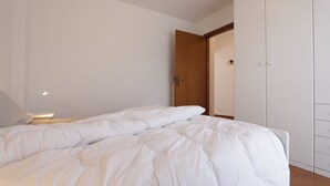 A bedroom with a bed, a nightstand, a wardrobe, and a door leading to another room.