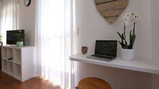 A room with a white desk, a laptop, a potted plant, and a heart-shaped decoration on the wall.
