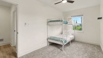 A room with a bunk bed, a ceiling fan, a window with a view, and a door.