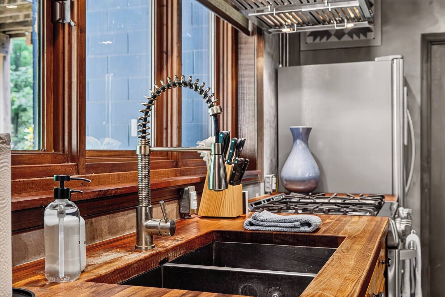 A kitchen with a wooden countertop, a stainless steel sink, a gas stove, and a vase on the counter.