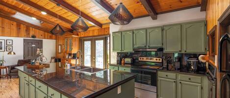 A spacious kitchen with wooden beams, green cabinets, and a central island.
