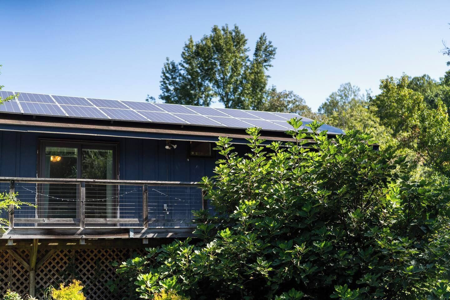 A house with a solar panel roof, a balcony, and dense greenery in the foreground.