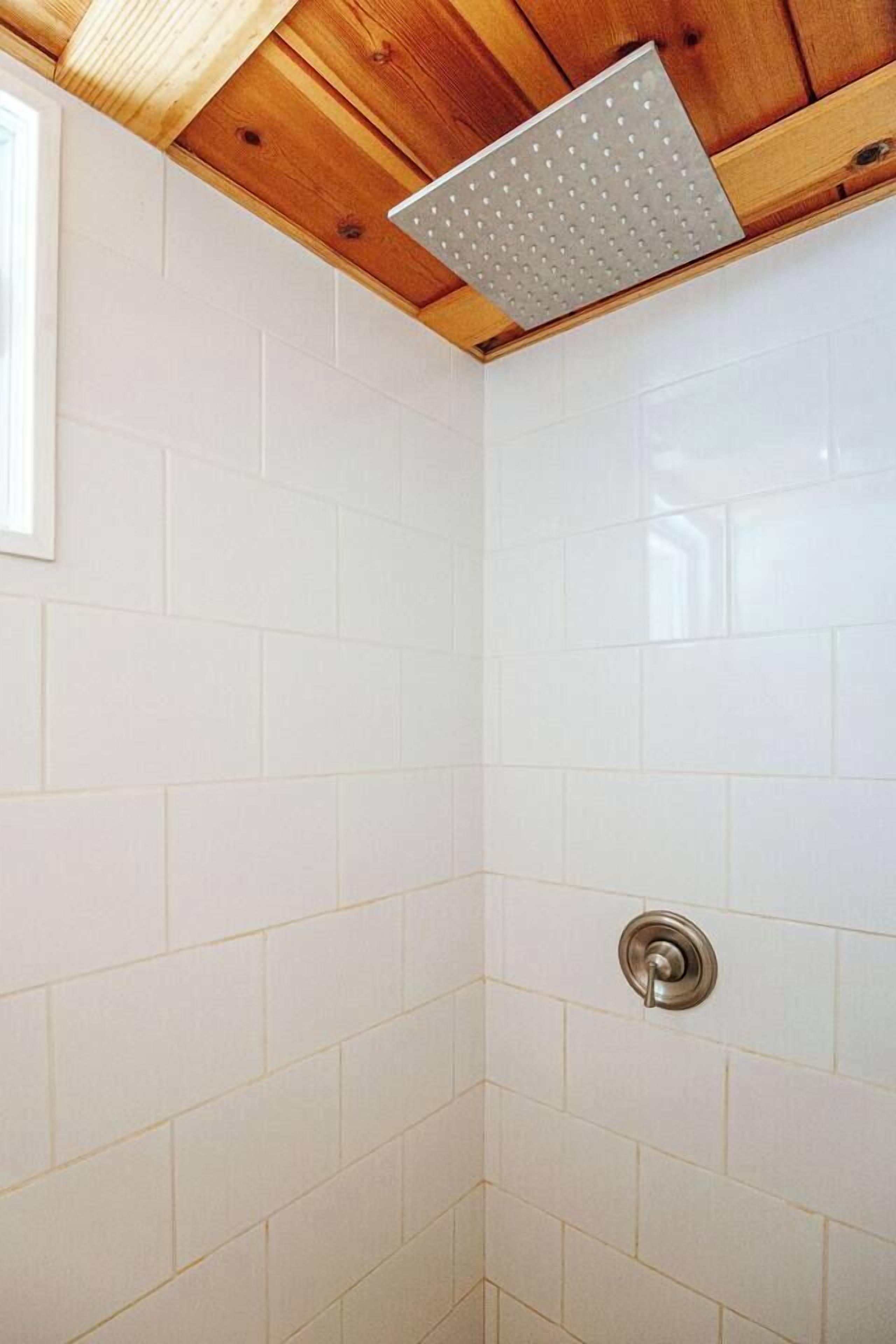 A shower with white tiles and a wooden ceiling.