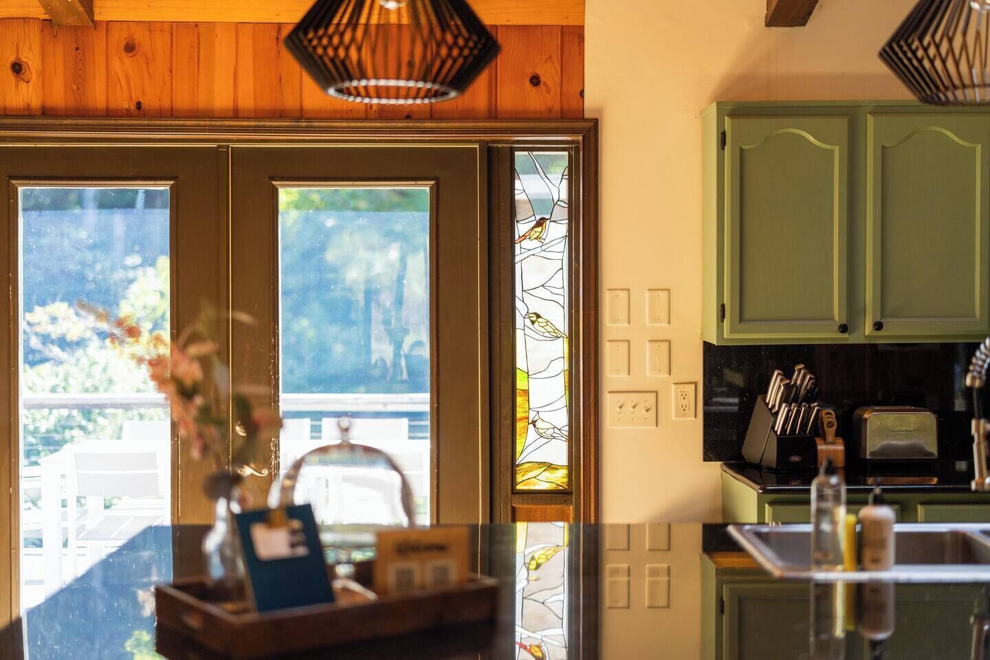 A kitchen with green cabinets, a countertop with a toaster, and a window with a view of greenery.