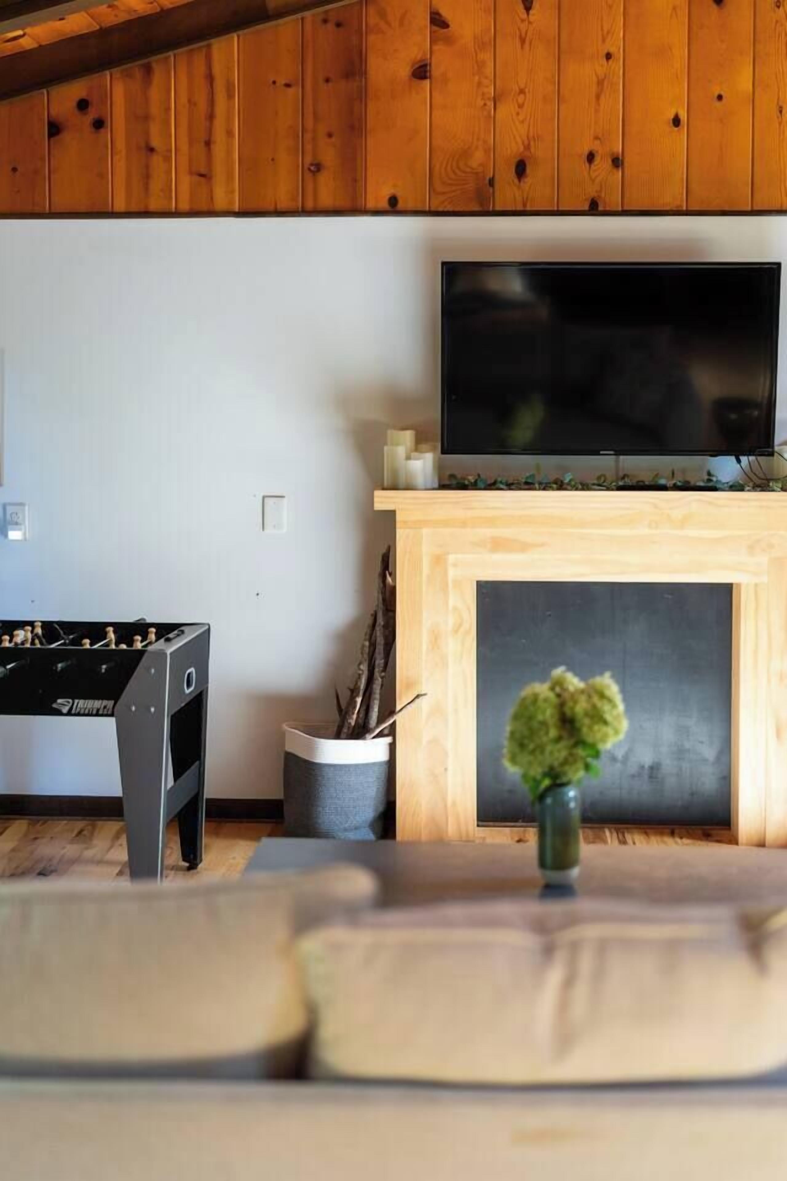 A room with a television mounted above a fireplace, a foosball table, and a small plant on a table.