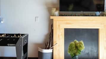 A room with a television mounted above a fireplace, a foosball table, and a small plant on a table.