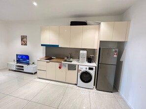 Une cuisine compacte équipée d’un lave-linge, d’un réfrigérateur et d’un téléviseur, le tout installé sur un meuble en marbre.