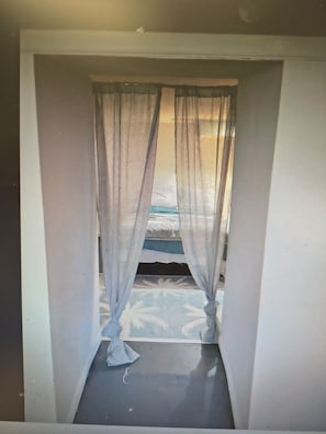 A room with a window featuring sheer curtains, a visible bed, and a view of a blue sky. - Cozy 1-bedroom apartment in fantastic Columbus with AC (Columbus)