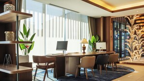 A modern hotel room with a desk, chairs, a computer, and a large window with curtains.