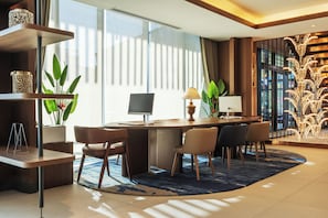 A modern hotel room with a desk, chairs, a computer, and a large window with curtains.
