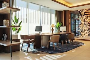 Quarto de hotel moderno com uma escrivaninha, cadeiras, um computador e uma janela grande com cortinas.