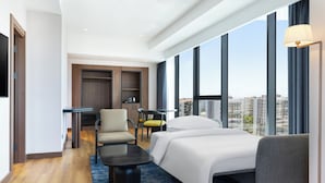 A hotel room with a bed, a desk, a chair, and a view of the city.