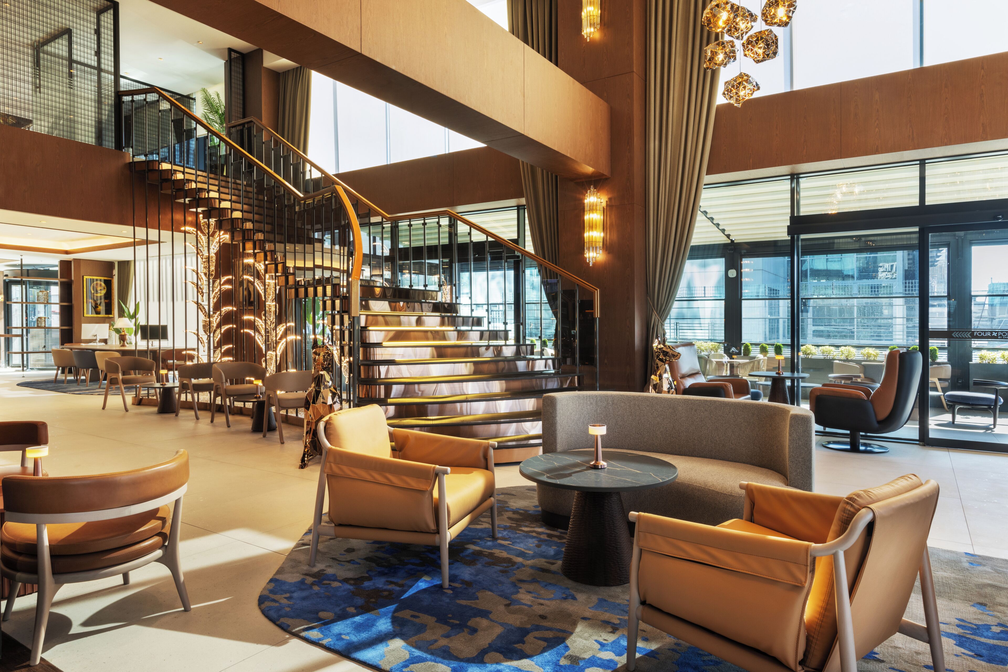 A spacious lobby with a modern staircase, comfortable seating areas, and large windows offering views of the city.