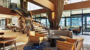 A spacious lobby with a modern staircase, comfortable seating areas, and large windows offering views of the city.