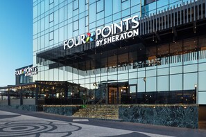 Un edificio moderno con fachada de vidrio y letreros de 'Four Points by Sheraton'.