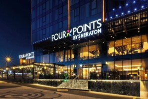 Fachada moderna de un hotel con señalización iluminada que dice 'FOUR POINTS BY SHERATON'.