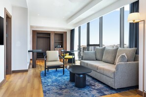 Una sala de estar moderna con un sofá, sillas, una mesa de centro y vistas de la ciudad a través de amplios ventanales.