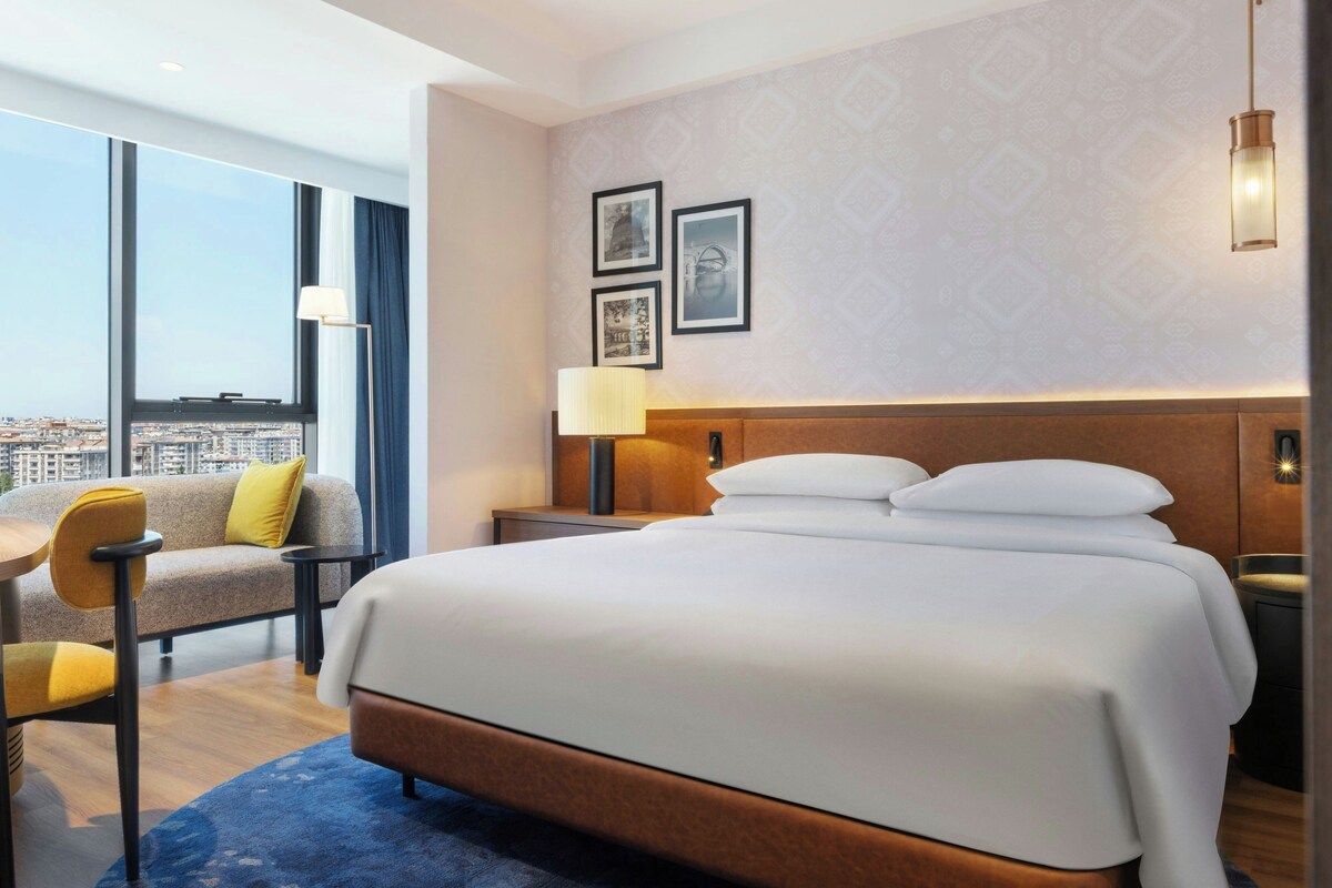 Una habitación de hotel con una cama grande, un escritorio, una silla y vistas a la ciudad.