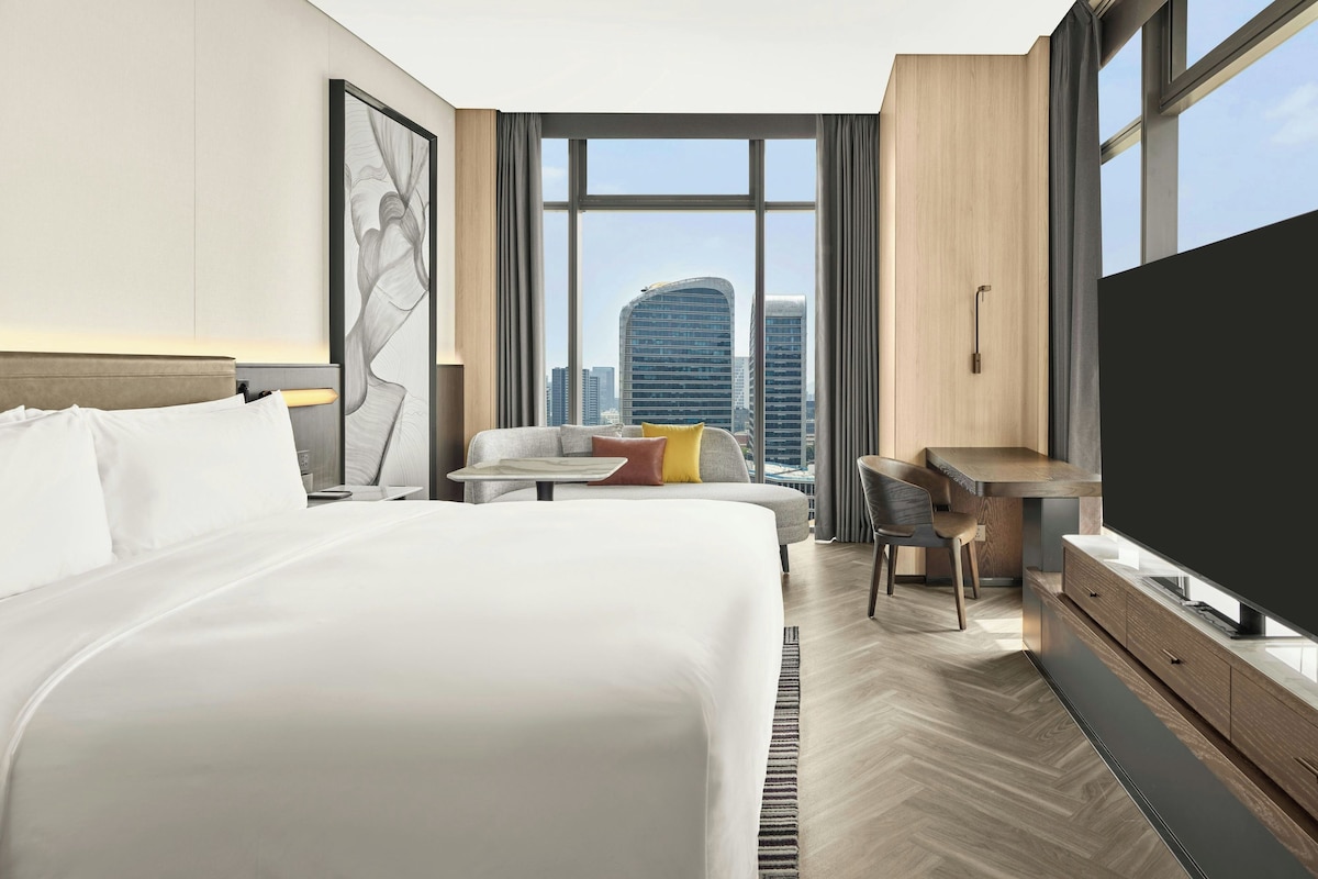 A modern hotel room with a large bed, a desk, a chair, and a TV.