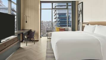 Ein modernes Hotelzimmer mit einem großen Bett, einem Schreibtisch, einem Sessel und einem Fernseher.