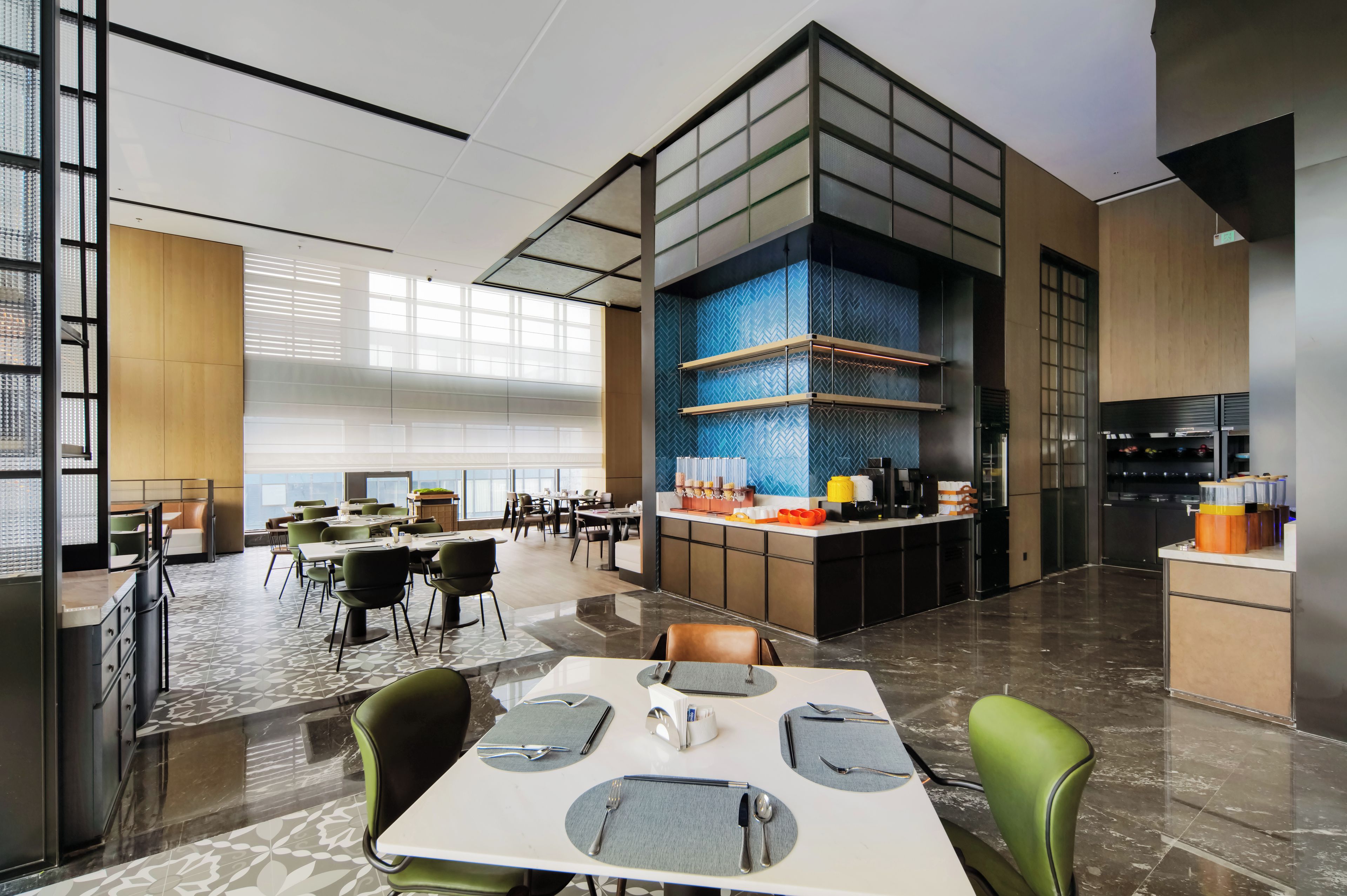 Un comedor moderno con mesas dispuestas para el servicio, un área de cocina con estación de café y un gran ventanal que proporciona luz natural.