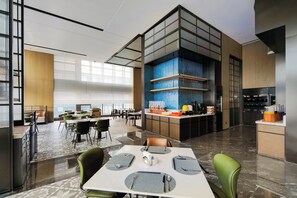 Un comedor moderno con mesas dispuestas para el servicio, un área de cocina con estación de café y un gran ventanal que proporciona luz natural.