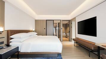 A modern hotel room with a large bed, a flat-screen TV, a bedside table, and a bench.
