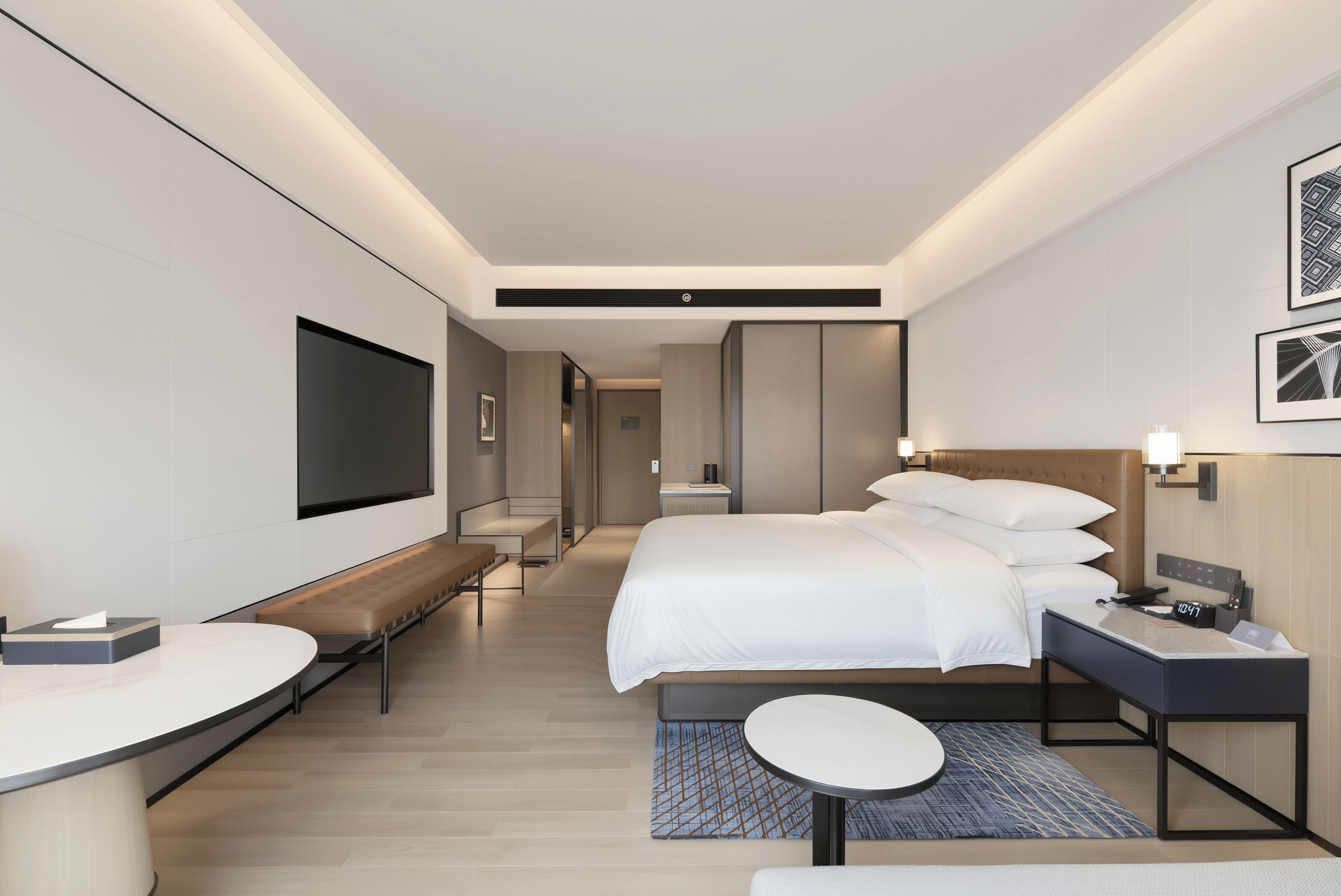 Une chambre d’hôtel moderne comprenant un lit, une table de chevet, un banc et une petite table ronde.