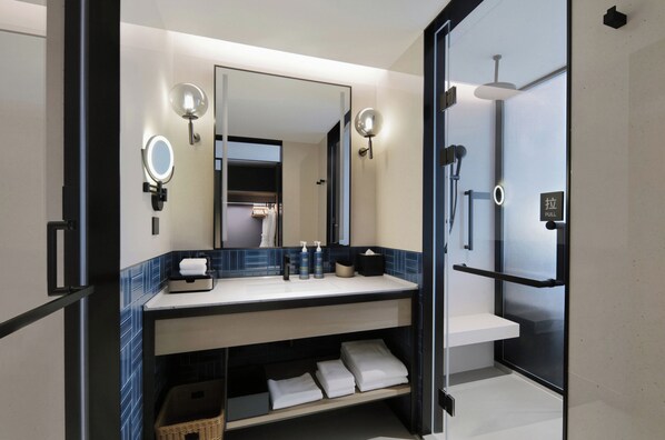 Un baño moderno con un espejo grande, dos luces empotradas, un perchero para toallas y una zona de ducha.
