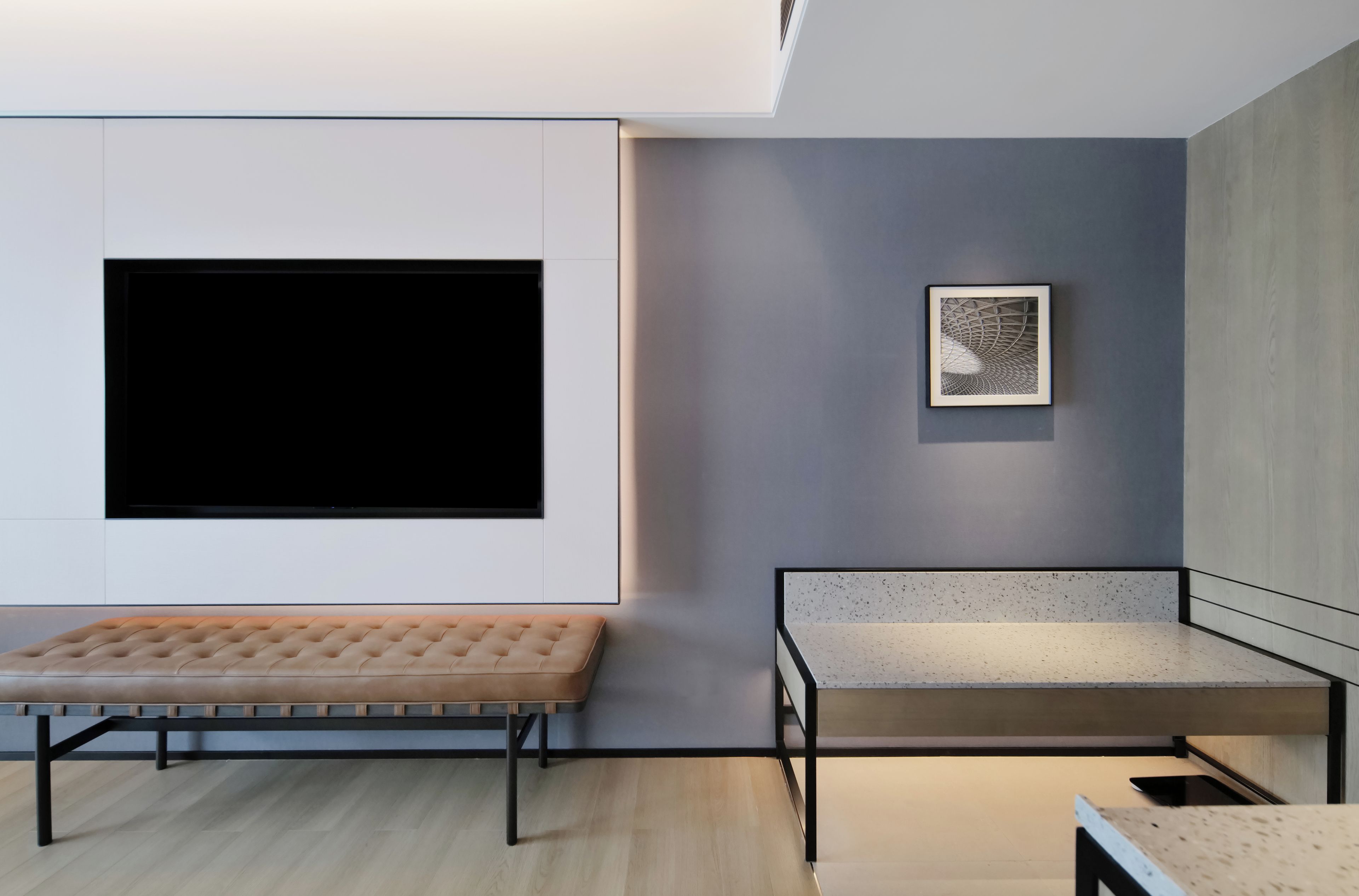 A modern living room with a large flat-screen TV mounted on the wall, a bench, and a small table.
