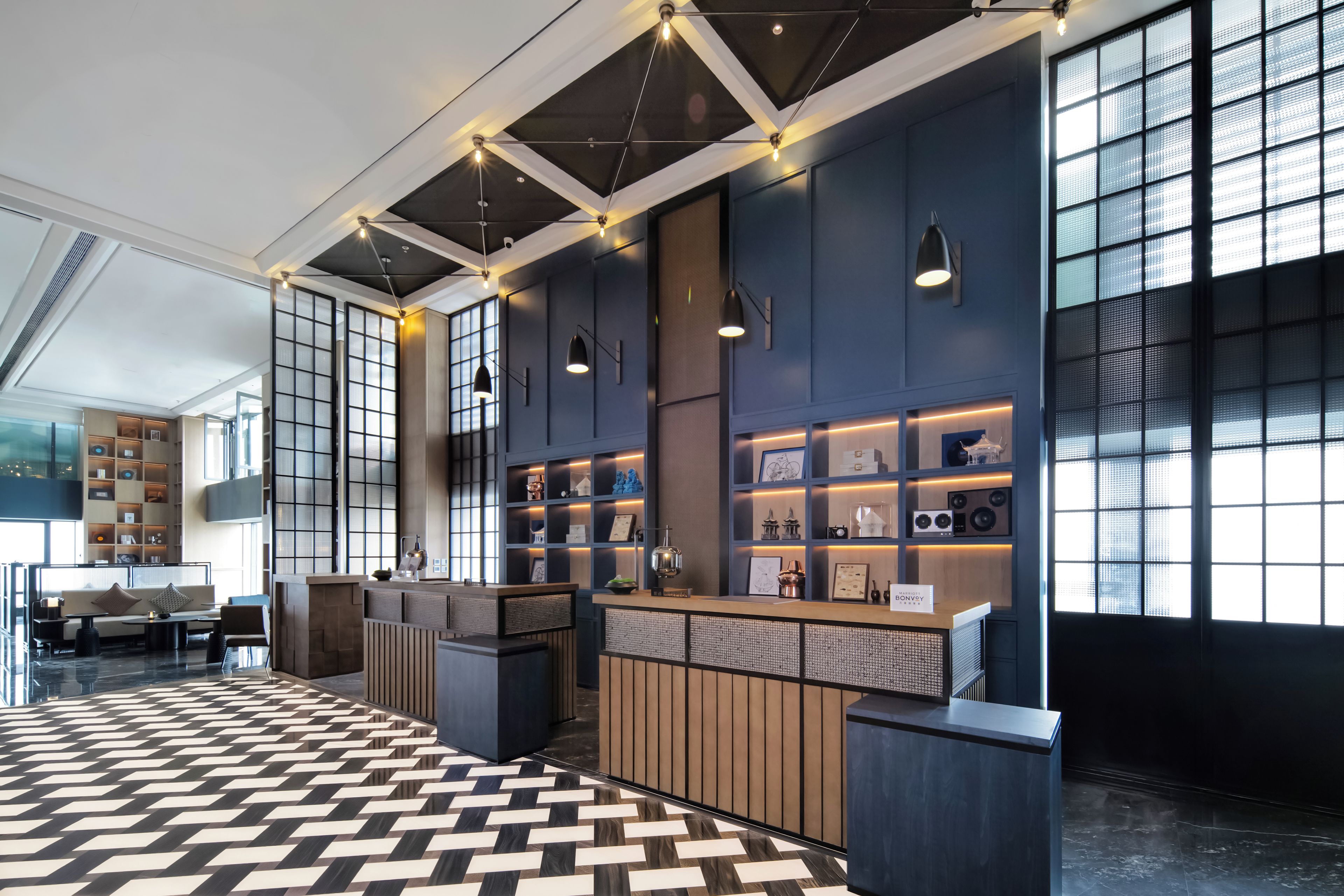 A modern hotel lobby with a check-in counter, seating area, and large windows.
