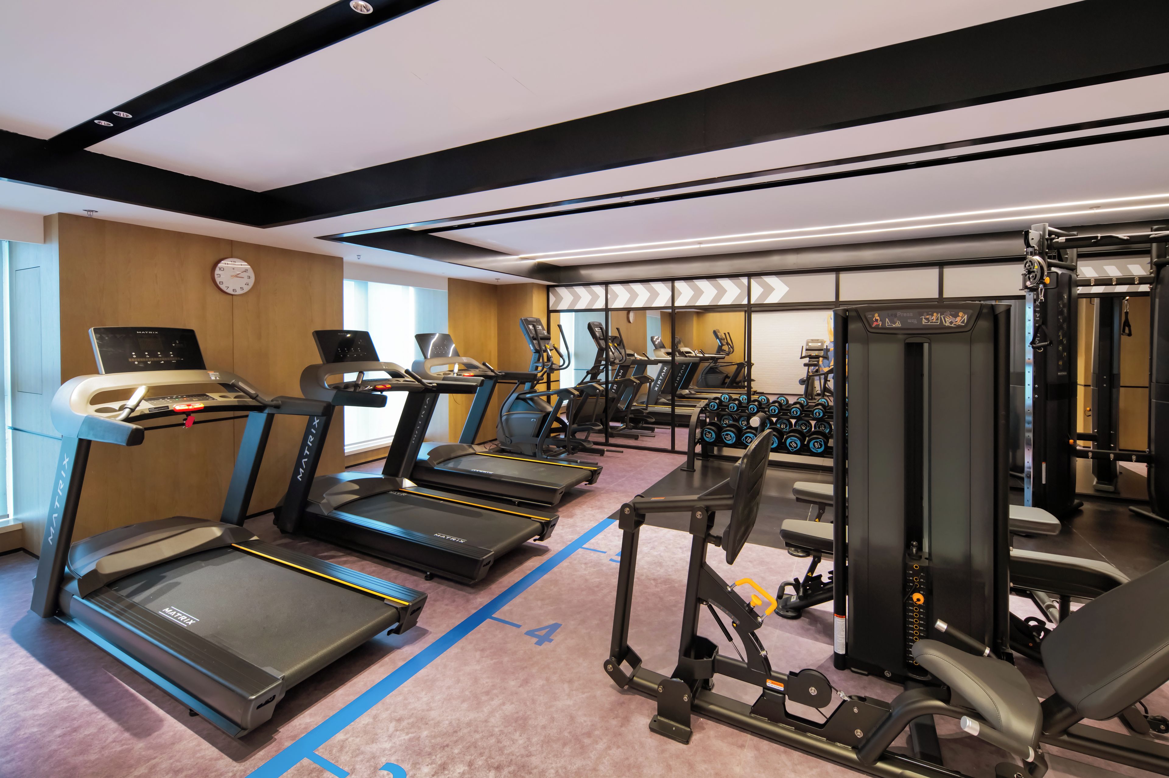 Un gimnasio con cintas de correr, máquinas de pesas y un reloj de pared.