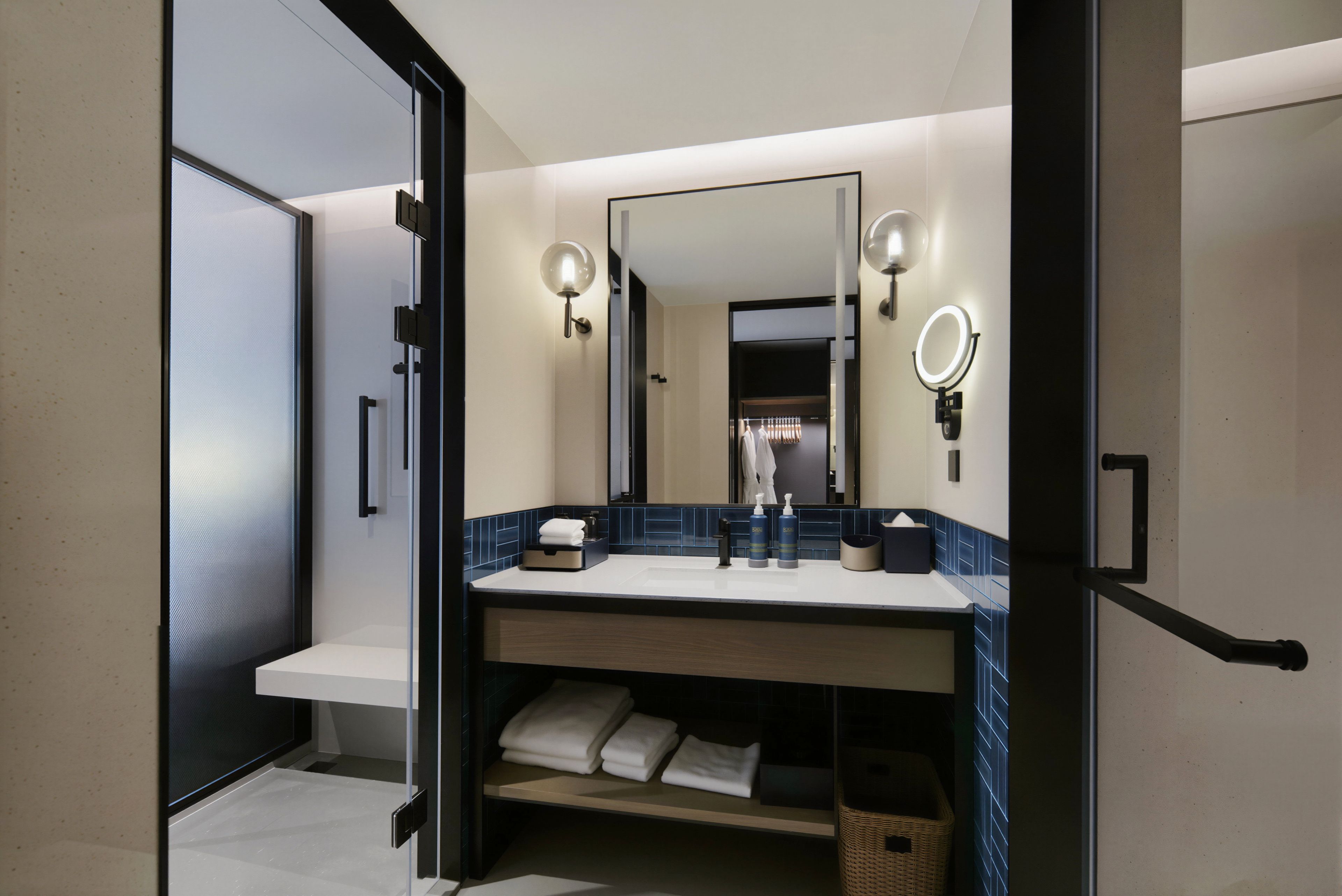 Un baño moderno con un espejo grande, dos luces empotradas, un lavamanos y un perchero para toallas.