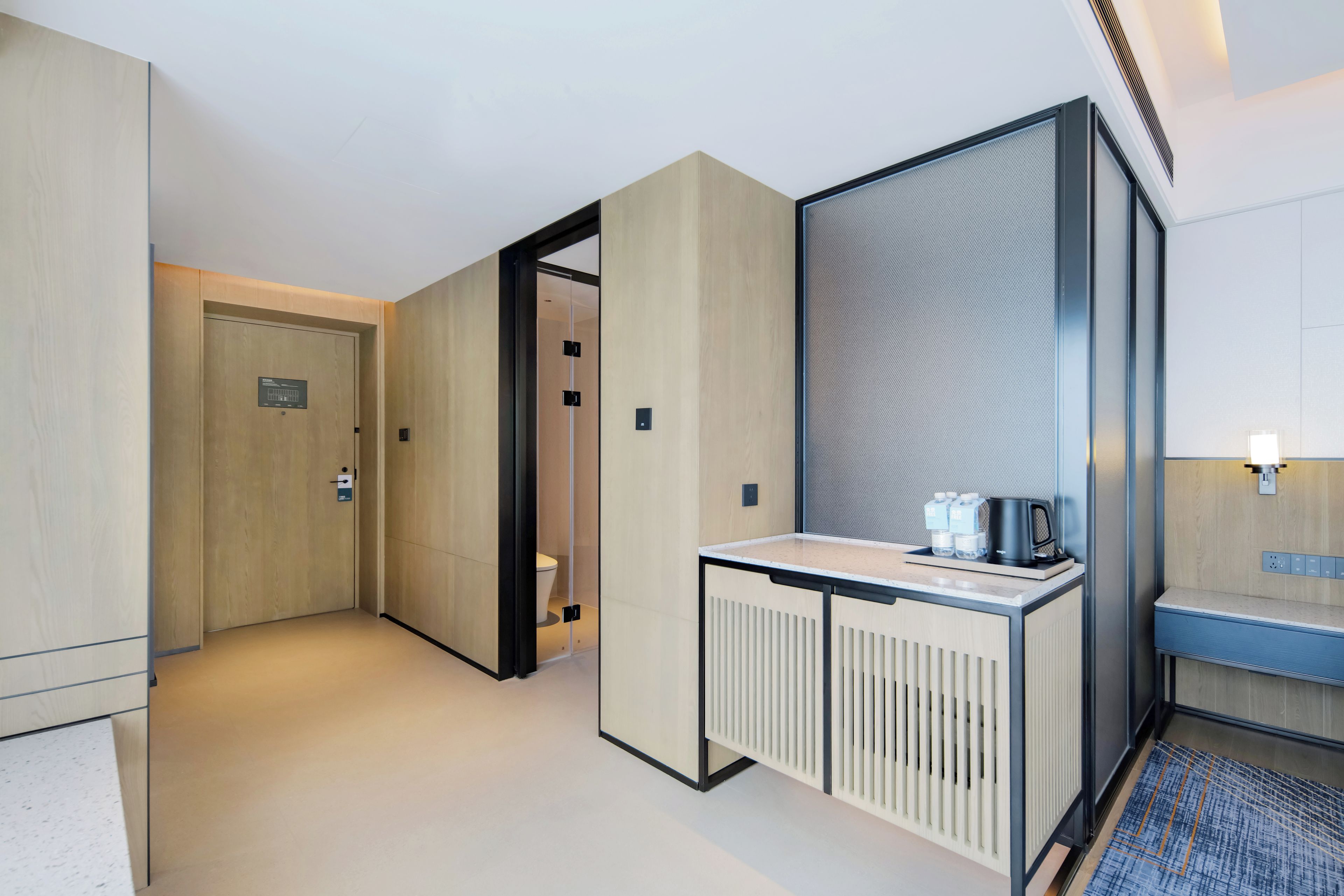 Corredor de hotel com mesa de recepção, banheiro privativo e porta de acesso a um quarto.