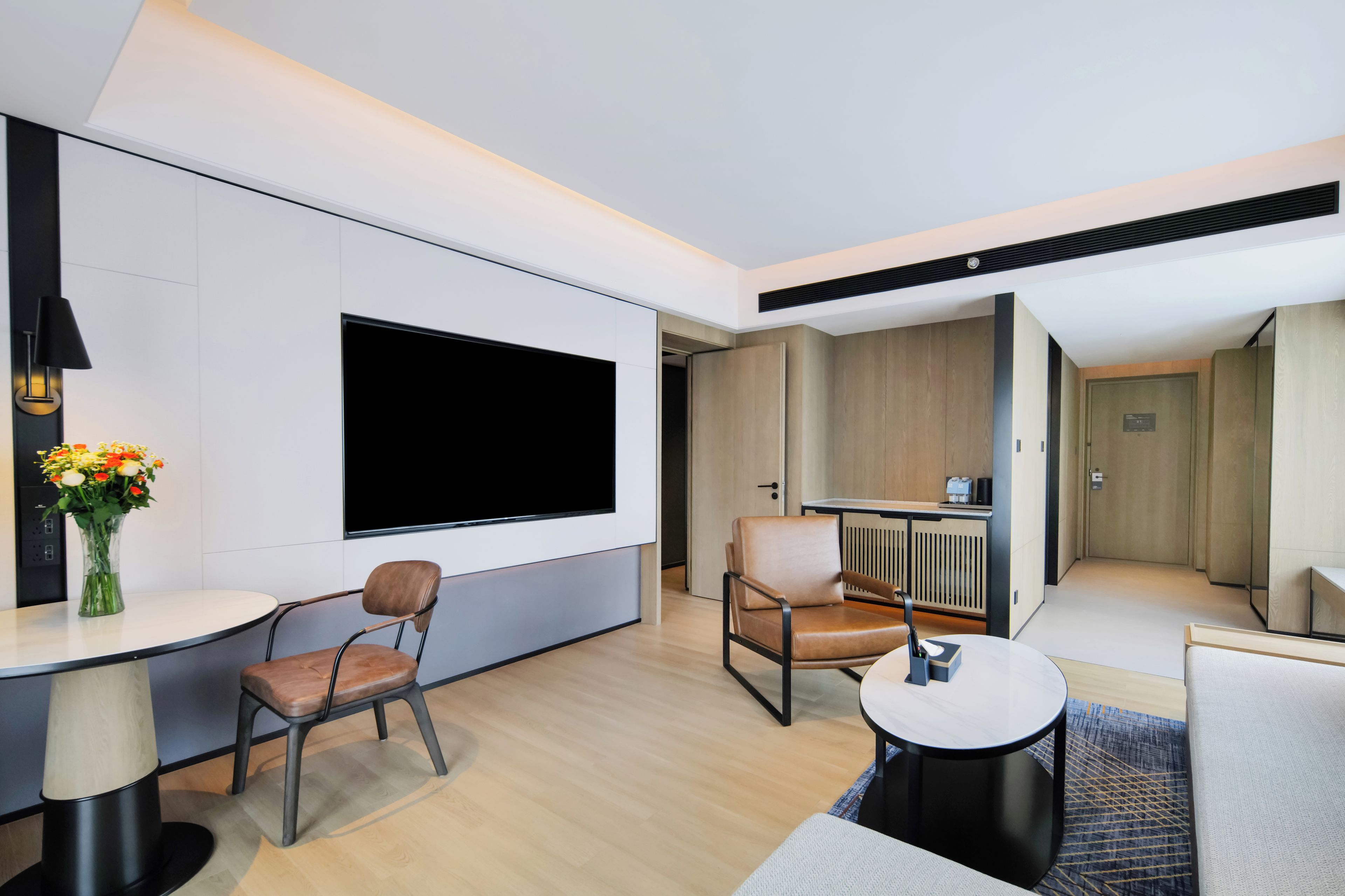 A modern hotel room with a flat-screen TV, two leather chairs, a small round table, and a coffee machine.