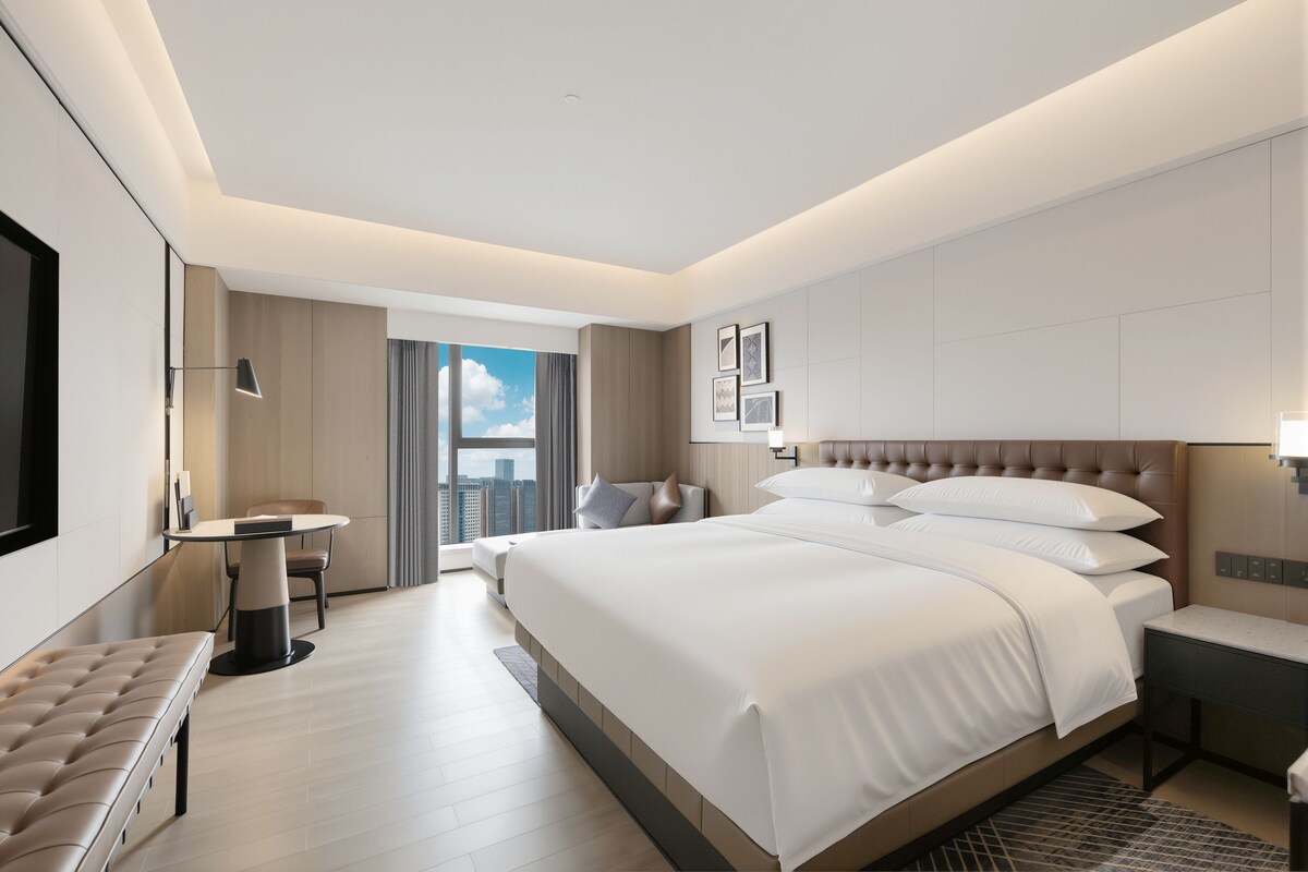 Habitación de hotel moderna con una cama grande, un escritorio, una silla y vistas de la ciudad.