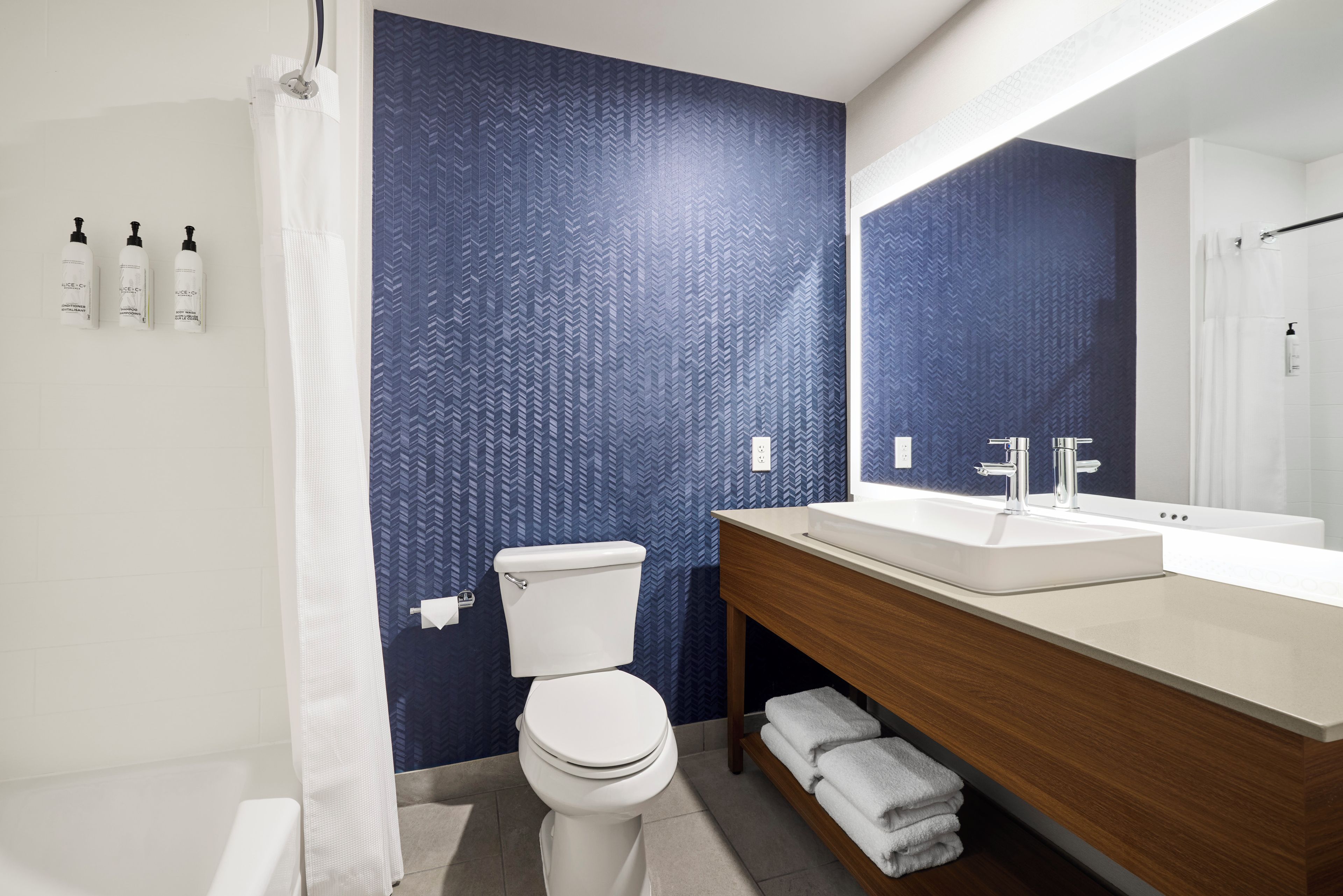 A modern bathroom with a white toilet, a sink with a mirror, and a blue patterned wall.