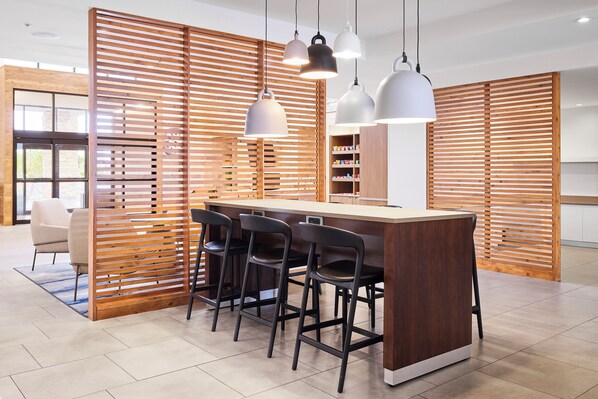 A modern kitchen with a wooden partition, bar stools, pendant lights, and a built-in shelf with snacks.