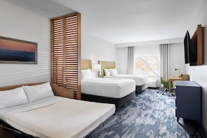 A hotel room with two beds, a desk, a chair, a TV, and a window with curtains.